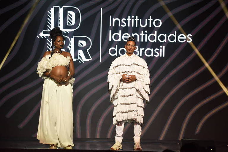 Duas pessoas negras em palco; elas vestem roupas brancas