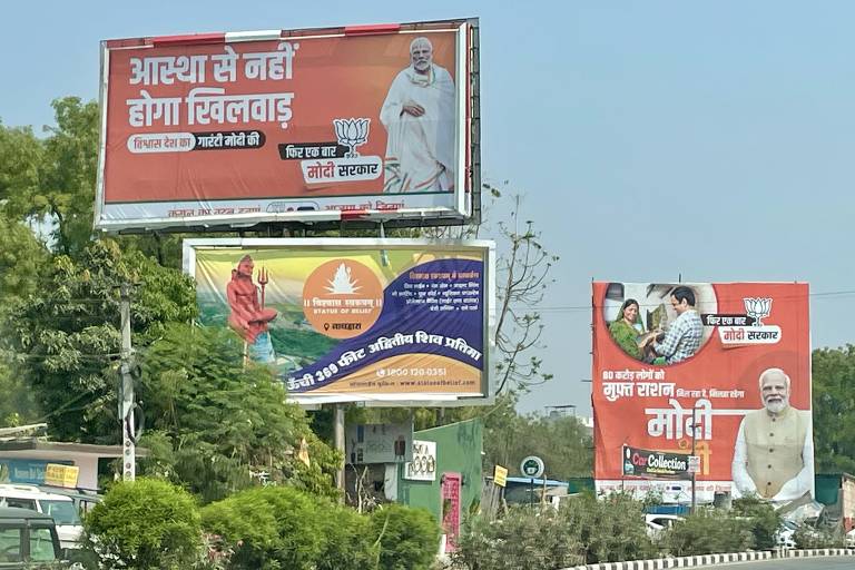 Outdoor em primeiro plano diz que 'A fé não será adulterada', com o selo 'Garantia de Modi', em Udaipur; em segundo plano, é propagandeada a distribuição de ração alimentar