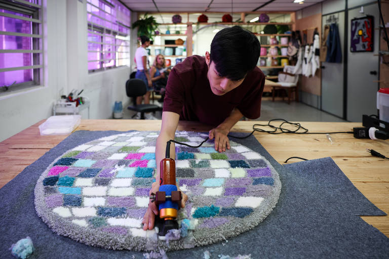 O artesão Christian Wang, 26, trabalha no acabamento de uma peça feita no workshop de tufting, técnica de tapeçaria, no estúdio Rug Lab, na Liberdade