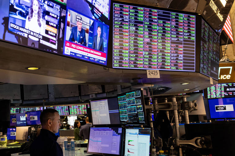 Trader trabalha dentro da cabine enquanto telas mostram as variações dos valores das ações .
