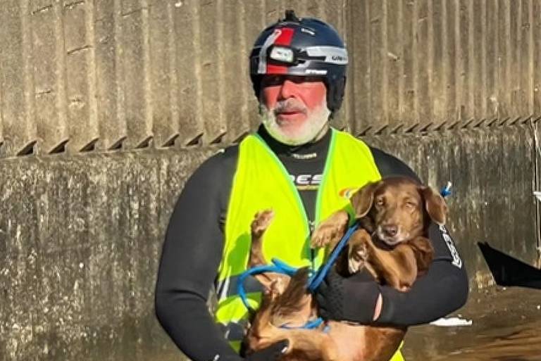 Em foto colorida, homem resgata um cachorro durante um enchente