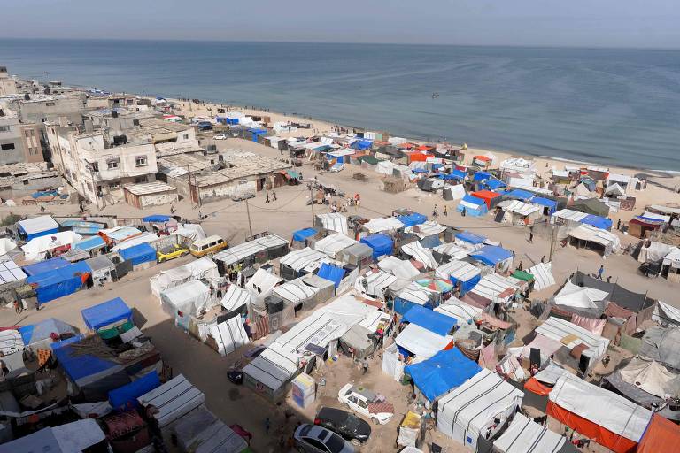 Um acampamento em uma praia com tendas de palestinos deslocados. Ao fundo é possível ver o mar calmo.