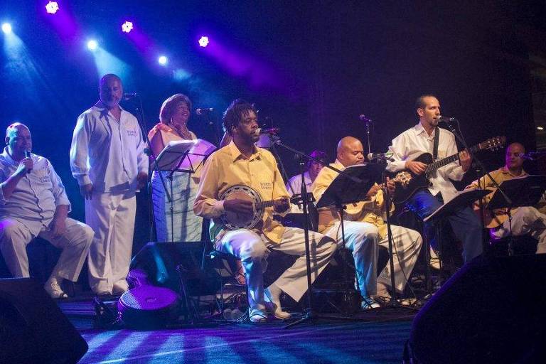 Em foto colorida, o grupo Berço do Samba de São Mateus aparece tocando em um palco