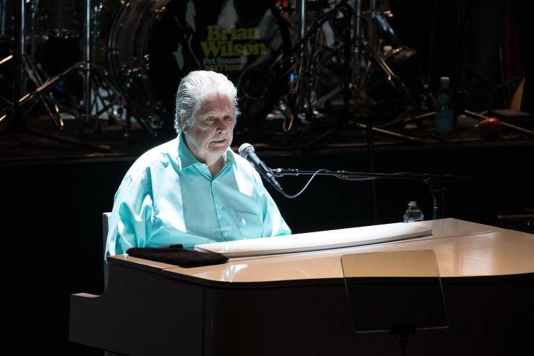 Homem de cabelos brancos e camisa azul sentado em frente a um piano