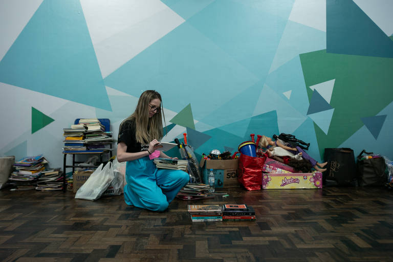 Na foto, Bárbara Puerari, psicóloga, mostra os livros e brinquedos que arrecadou para o abrigo montado no Colégio Rainha do Brasil, que recebe atualmente em torno de 200 pessoas, vítimas das enchentes no RS.