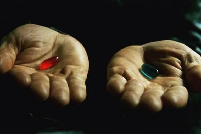 Duas mãos; em cada uma delas, uma pílula, vermelha e azul
