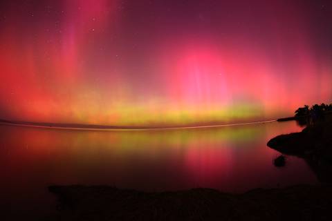 The Aurora Australis, also known as the Southern Lights, glow on the horizon over waters of Lake Ellesmere on the outskirts of Christchurch on May 11, 2024. The most powerful solar storm in more than two decades struck Earth, triggering spectacular celestial light shows from Tasmania to Britain -- and threatening possible disruptions to satellites and power grids as it persists into the weekend. (Photo by Sanka Vidanagama / AFP)
