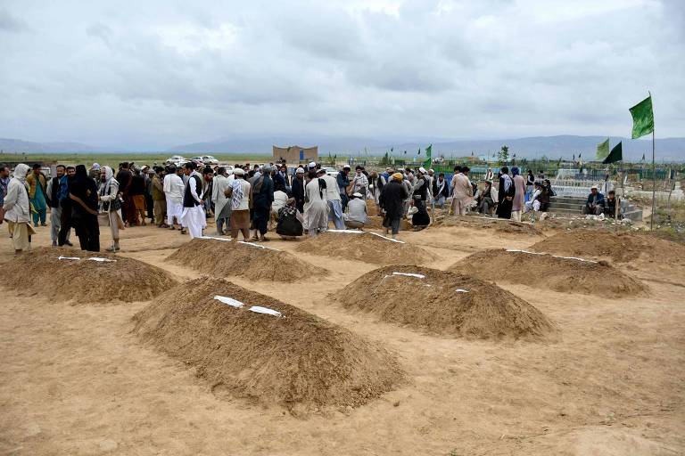 Imagem mostra montes de terra onde foram enterrados corpos e pessoas ao fundo