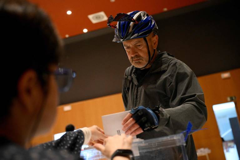 Eleitor com capacete de bicicleta deposita seu voto em urna de papel, na Catalunha, Espanha