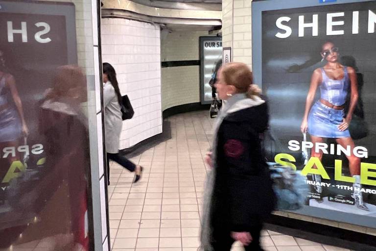 Mulher passa na frente de propaganda da Shein em estação de metrô. Fornecedores da Shein ainda trabalham 75 horas por semana, diz relatório. A Shein disse que está fazendo "progressos significativos na melhoria das condições"

