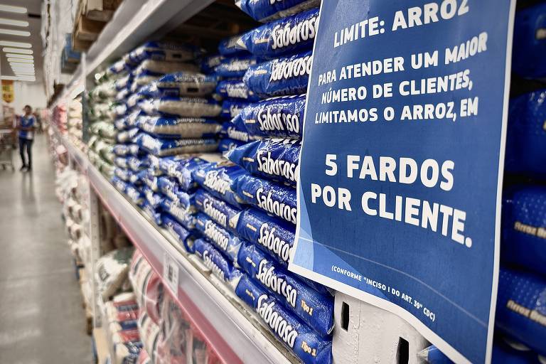 Cartaz azul em prateleira de supermercado avisa que compra de arroz é limitada a 5 fardos por clientes
