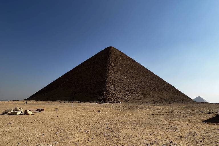 A imagem captura a Grande Pirâmide de Gizé sob um céu azul claro, com sua estrutura dominando a paisagem desértica
