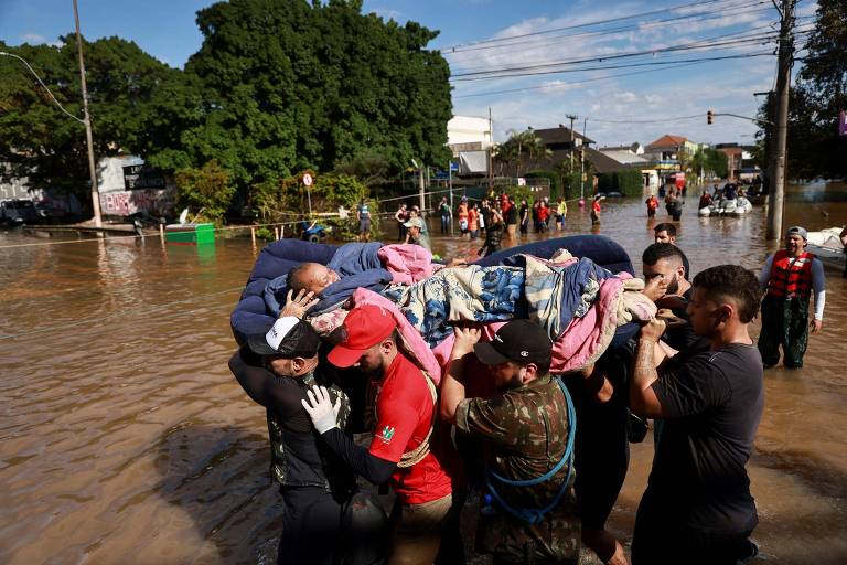 Mulher sendo carregada por socorristas após sua casa ser inundada em Porto Alegre