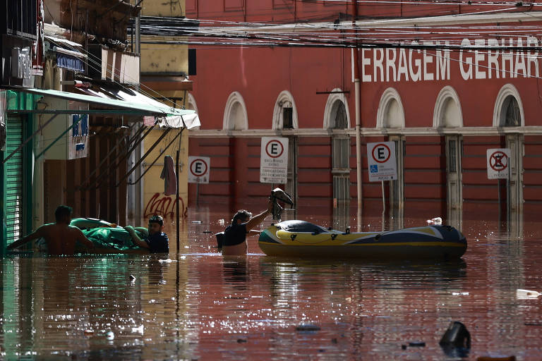 Homens passam por região alagada de Porto Alegre em barco inflável; as águas do lago Guaíba estão baixando, mas muitas ruas ainda estão embaixo d'água