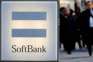 FILE PHOTO: People walk behind the logo of SoftBank Corp in Tokyo