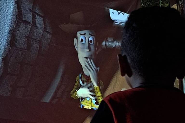 Na foto, uma criança de costas assiste ao filme Toy Story projetado em um telão