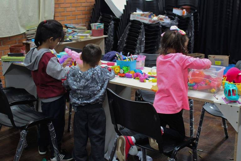 Na foto, três crianças brincam em uma mesa com brinquedos