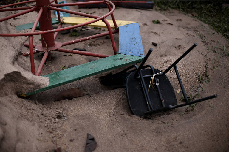 Restos de materiais escolares como carteiras e gira-gira estão parcialmente soterrados na areia, lavada por águas das chuvas