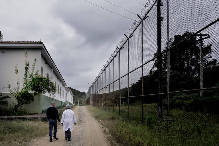 Diretor do hospital e enfermeira chefe andam ao lado de grades na parte interna da ala masculina da instituição