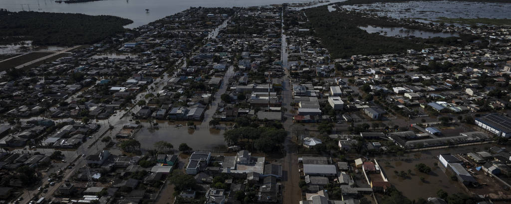 A imagem mostra uma vista aérea de uma cidade parcialmente submersa em água, com ruas e casas inundadas
