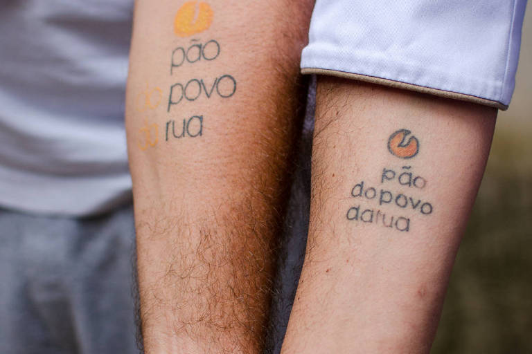 braços com tatuagens que dizem Pão do Povo da Rua  
