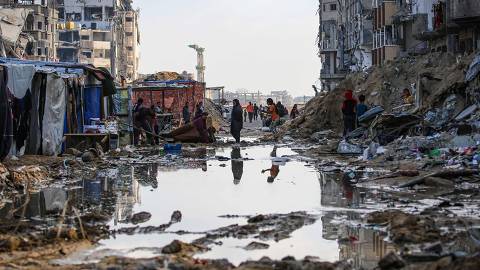 TOPSHOT - Displaced Palestinians walk around a puddle in front of destroyed buildings and tents in Khan Yunis in the southern Gaza Strip on May 16, 2024, amid the ongoing conflict between Israel and the militant group Hamas. (Photo by AFP)