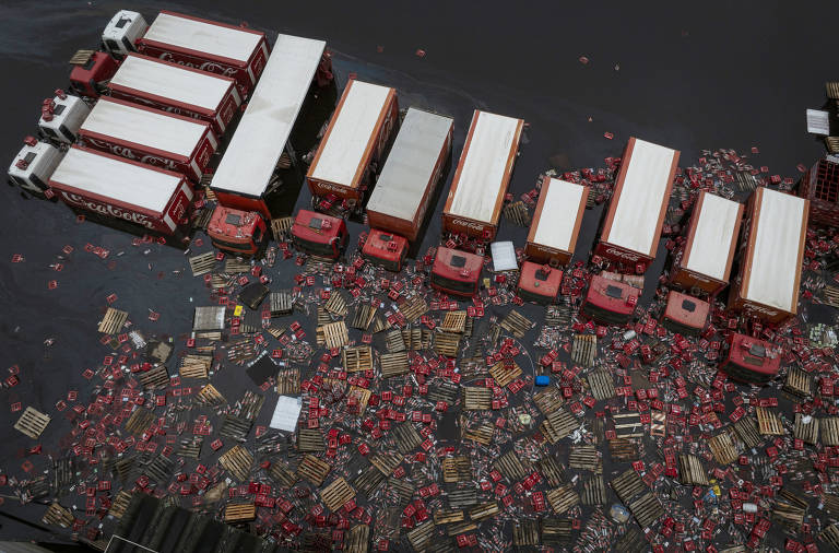 Imagem aérea mostra caminhões, caixas de refrigerante e garrafas boiando