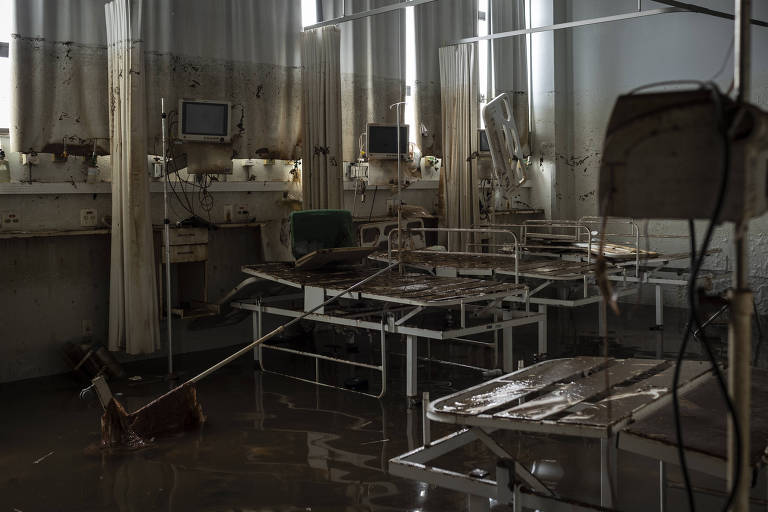 Hospital abandonado com macas e equipamentos coberto de barro.