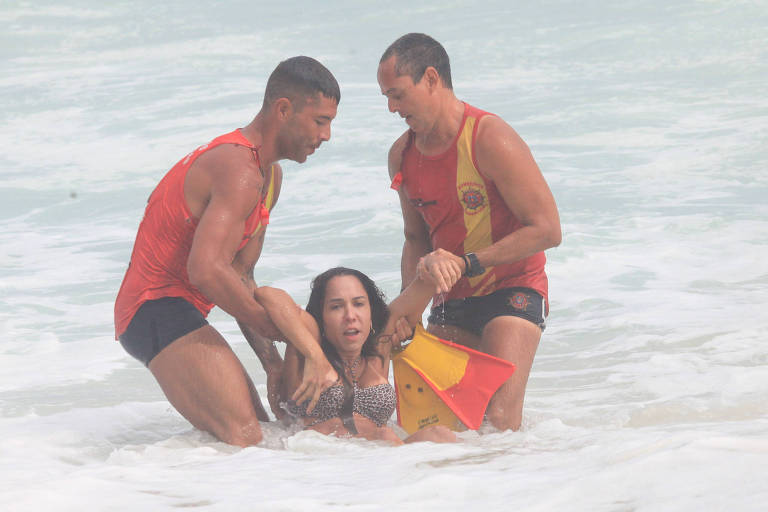 Em foto colorida, dois homens salvam uma mulher no mar