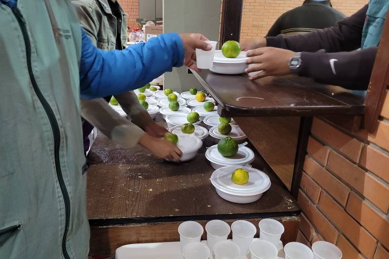 Na foto, pessoas recebem marmitas com uma fruta