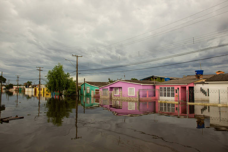 Na foto, casas coloridas estão parcialmente alagadas. A água cobre o chão, e reflete o céu nublado