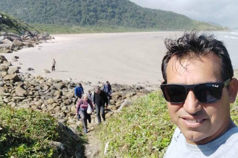 Homem com óculos com praia da Ilha do Cardoso ao fundo