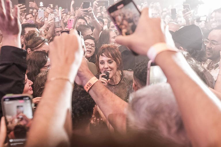A cantora Zaz, com cabelo curto, é cercada por fãs durante performance no meio da plateia. Enquanto ela canta, a multidão registra o momento com seus celulares