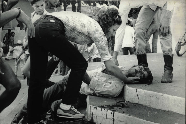 Imagem em preto e branco mostra uma mulher observando o metalúrgico aposentado Amaral Meloni, caído numa escadaria após sofrer um tiro na cabeça em Guariba, cidade do interior de São Paulo