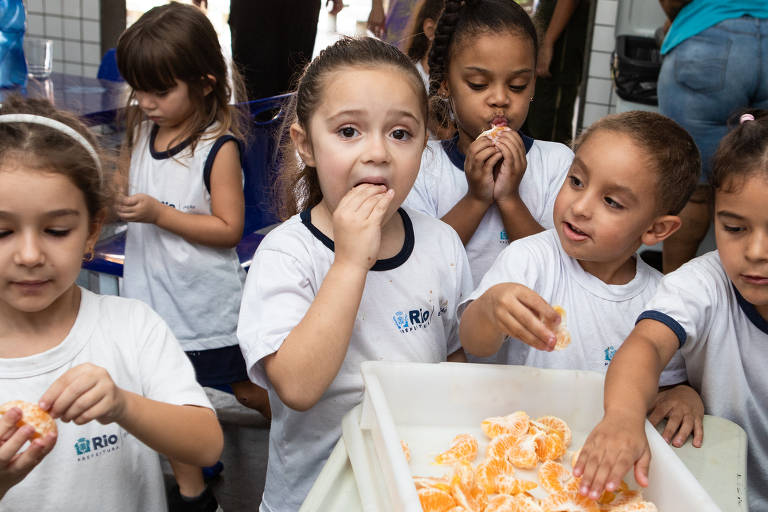 Grupo de crianças uniformizadas comem tangerina na hora do almoço na escola municipal Roberto Burle Marx, em Curicica, no Rio