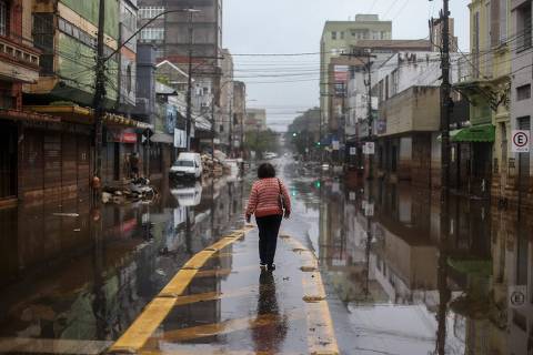 A woman walks through a flooded street in Porto Alegre, Rio Grande do Sul State, Brazil, on May 24, 2024. The key agricultural state of Rio Grande do Sul has been hit by an unprecedented climate disaster for the past three weeks, with cities and rural areas alike inundated by torrential rains that have left more than 150 people dead and some 100 missing. (Photo by Anselmo Cunha / AFP)