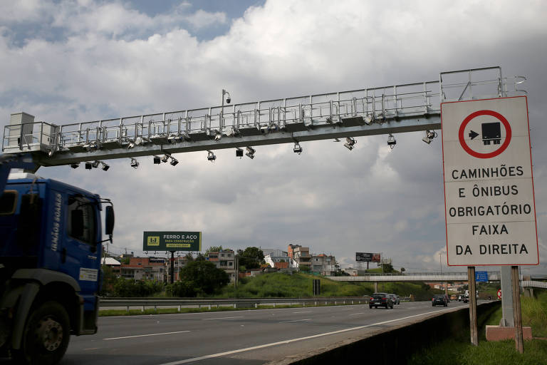estrutura de metal com câmeras forma arco sobre rodovia por onde passa um caminhão.