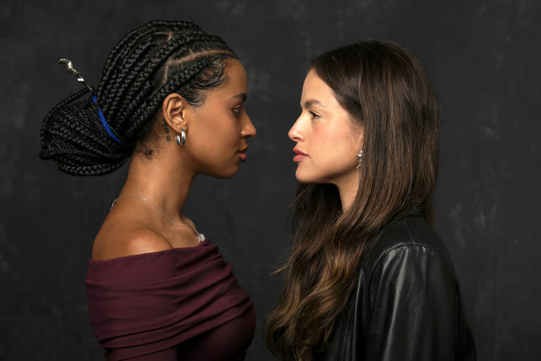 Uma mulher negra de cabelos pretos e uma mulher branca de cabelos castanhos. Elas estão cara a cara
