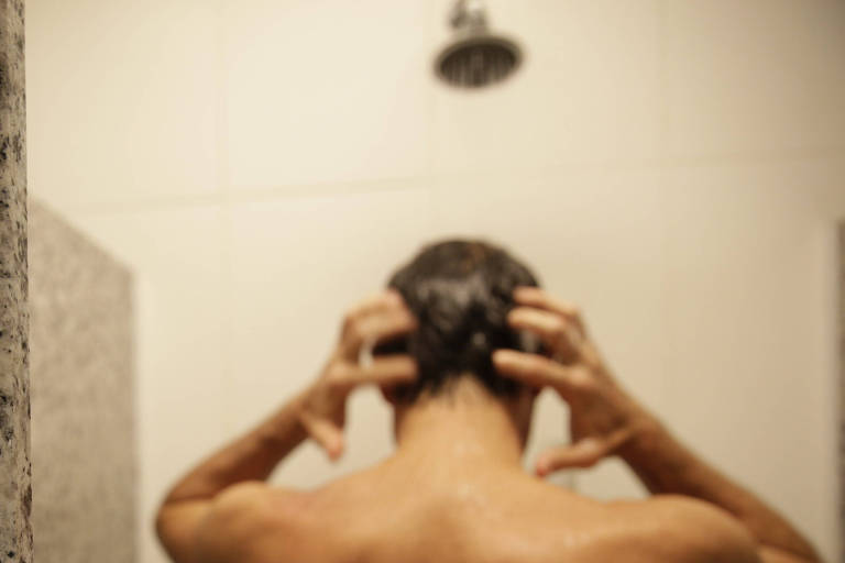 Homem toma banho ao lado de placa, que informa que o chuveiro economiza água