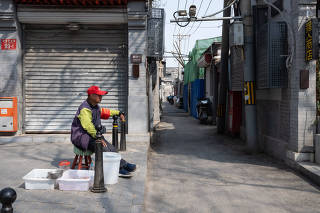 A volunteer from a neighborhood committee keeps watch along a street while also feeding goldfish in Beijing, April 3, 2024. (Gilles Sabri/The New York Times)