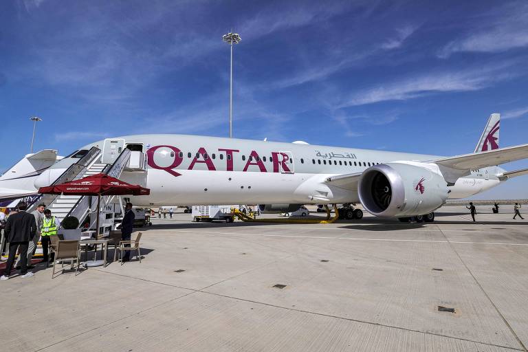 Foto mostra uma aeronave branca parada em um pátio, estampada com o logo da companhia Qatar Airways, cujas letras são na cor vinho