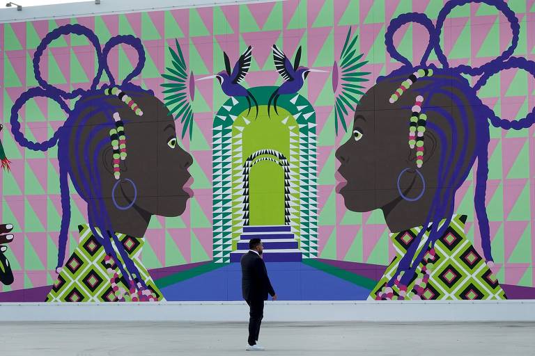 Um indivíduo passa por mural, no qual duas figuras femininas negras estilizadas em perfil, com tranças em seus cabelos roxos, enquadram uma escadaria colorida que leva a um "portal"