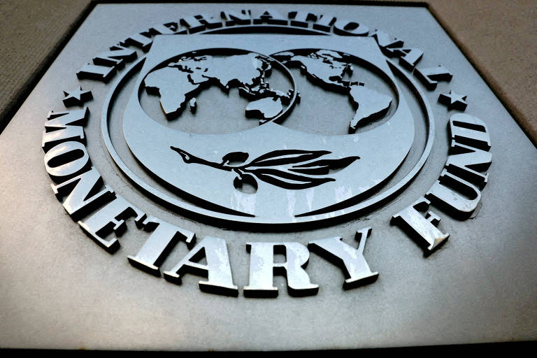 A imagem mostra um emblema metálico em relevo com as palavras "MONETARY FUND" em destaque, indicando que se trata do símbolo do Fundo Monetário Internacional (FMI). O emblema apresenta um globo terrestre cercado por um raminho de oliveira.