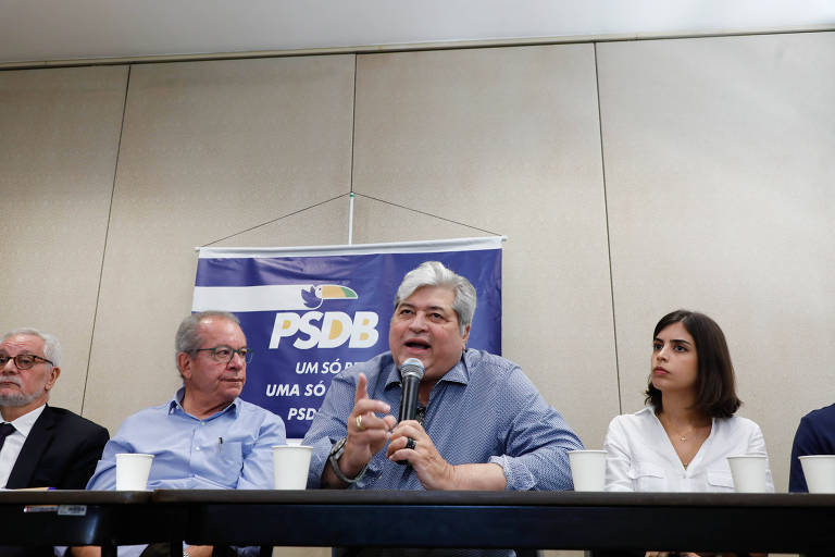 Fotografia de Datena e Tabata Amaral em evento de filiação do apresentador ao PSDB. Datena veste camisa social azul e Tabata, camisa social branca
