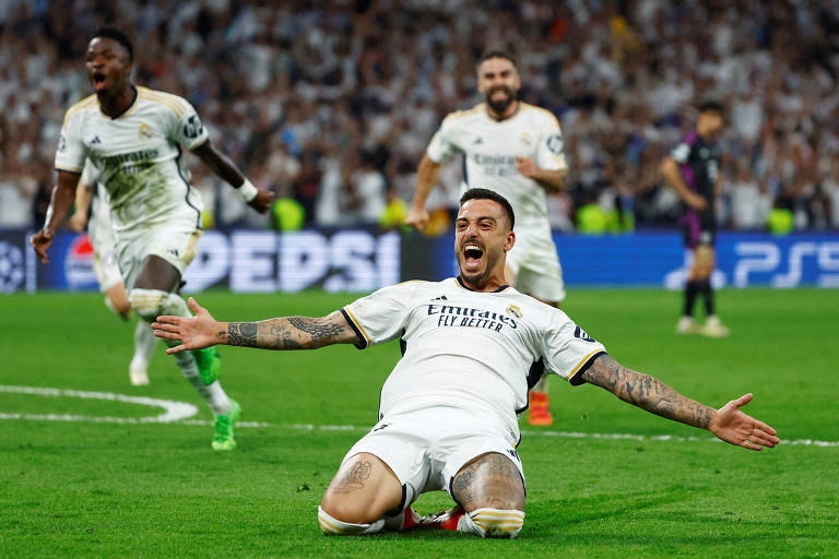 Joselu, do Real Madrid, comemora o segundo gol deslizando de joelhos pelo gramado com os braços abertos em um estádio lotado, enquanto seus companheiros de equipe correm em sua direção para celebrar o feito