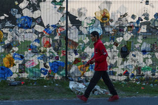 Plastic waste and other pieces of litter are blown against a fence in Cape Town
