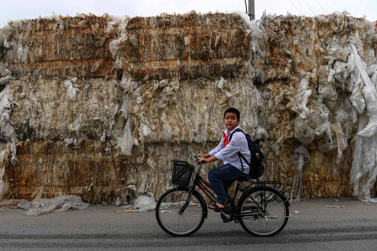 VIETNAM - Criança volta da escola diante de pilhas de resíduos plásticos separados em fardos para reciclagem na província de Hung Yen