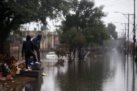 TOPSHOT - Men look at a  flooded street in the Sarandi neighborhood, one of the hardest hit by the heavy rains in Porto Alegre, Rio Grande do Sul state, Brazil, on May 27, 2024. Cities and rural areas alike in Rio Grande do Sul have been hit for weeks by an unprecedented climate disaster of torrential rains and deadly flooding. More than half a million people have fled their homes, and authorities have been unable to fully assess the extent of the damage. (Photo by Anselmo Cunha / AFP)
