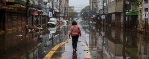 A woman walks through a flooded street in Porto Alegre, Rio Grande do Sul State, Brazil, on May 24, 2024. The key agricultural state of Rio Grande do Sul has been hit by an unprecedented climate disaster for the past three weeks, with cities and rural areas alike inundated by torrential rains that have left more than 150 people dead and some 100 missing. (Photo by Anselmo Cunha / AFP)