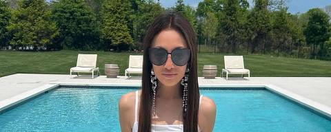 Vera Wang em foto no Instagram *** Local Caption *** Uma mulher estilosa senta-se à beira de uma piscina cristalina, exibindo óculos de sol grandes e sandálias decoradas. Seu olhar confiante e a postura relaxada complementam o cenário luxuoso de um dia ensolarado.